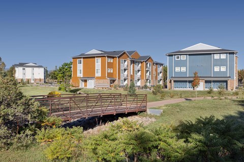 A bridge crosses a grassy area in front of a row of apartment buildings.