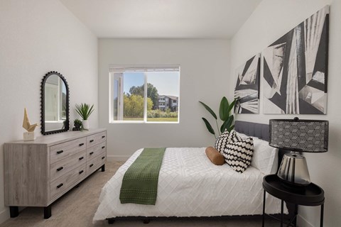 A bedroom with a bed, dresser, and a large window.