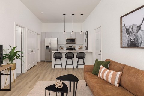 A living room with a brown couch and a black coffee table and a kitchen in the back.