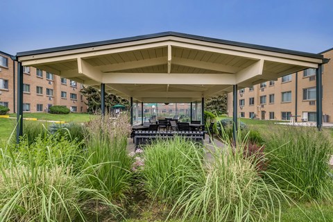 A covered patio area with a table and chairs in front of apartment buildings.