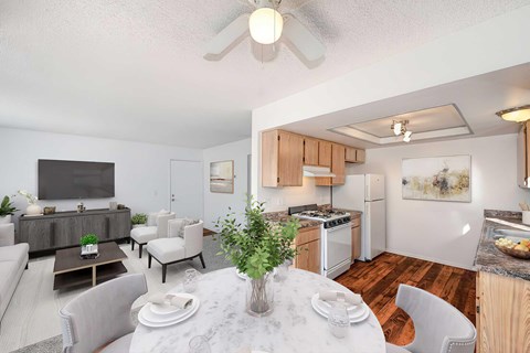 A kitchen and dining room with wood style plank flooring, faux granite countertops, and a ceiling fan, The room is staged with artwork, a rug, and a set dining room table.