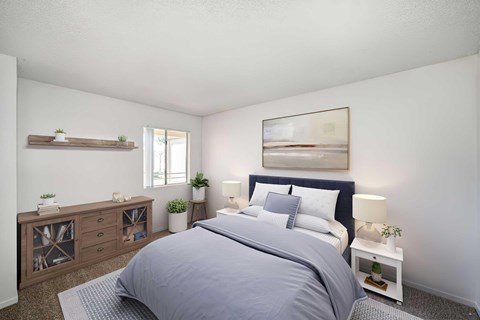 A bedroom with white walls, carpet, and a window. The room is staged with a bed, artwork, and a TV stand.