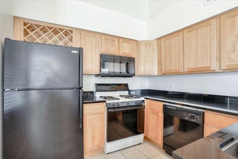 A black refrigerator is in a kitchen with wooden cabinets.