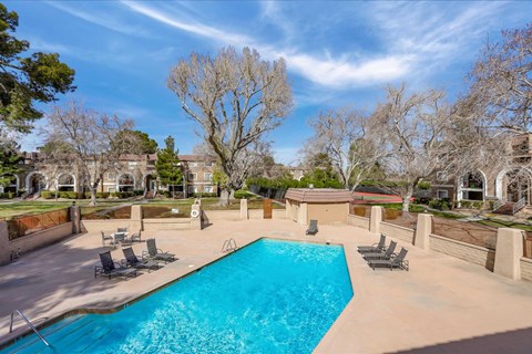 A large swimming pool surrounded by a concrete patio and lounge chairs.