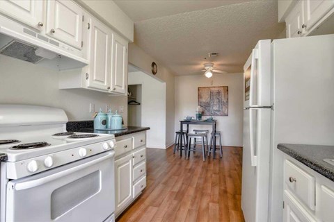 A kitchen with a stove, refrigerator, and a dining table with chairs.