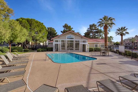 A pool surrounded by lounge chairs and a house in the background.