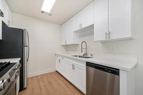 The kitchen of the renovated apartments with stainless steel appliances, wood style plank flooring, white cabinets, and faux marble countertops.