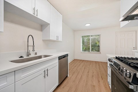 The kitchen of the renovated apartments with stainless steel appliances, wood style plank flooring, white cabinets, and faux marble countertops.