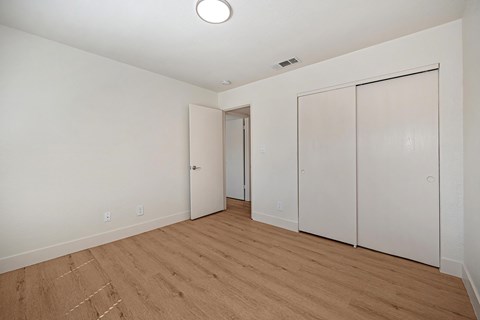 The bedroom of the renovated apartments with wood style plank flooring, white walls, and a closet.