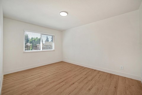 The bedroom of the renovated apartments with wood style plank flooring, white walls, and a window.