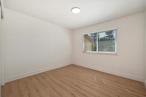 The bedroom of the renovated apartments with wood style plank flooring, white walls, and a window.