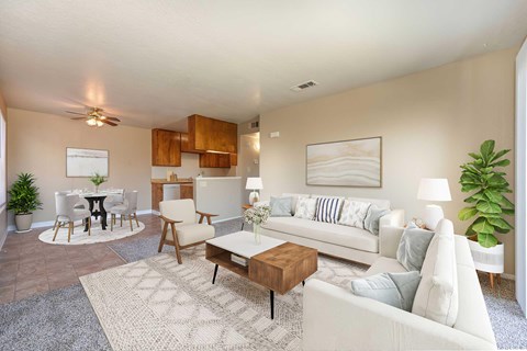 The living room of the classic interiors with carpet and off white walls. The room is staged with a couch, chairs, a rug, coffee table, and a tv.