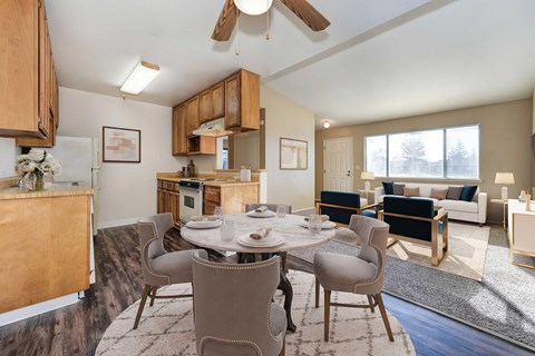 An overview of the kitchen and dining room area with a dining room table set for 4 people. There is a ceiling fan above the table and the cabinets are wooden.