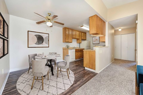 An overview of the kitchen and dining room area with a dining room table set for 4 people. There is a ceiling fan above the table and the cabinets are wooden.