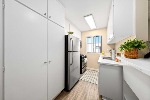A kitchen with white cabinets, vinyl flooring, stainless front appliances, quartz countertops, and a small window with blinds.
