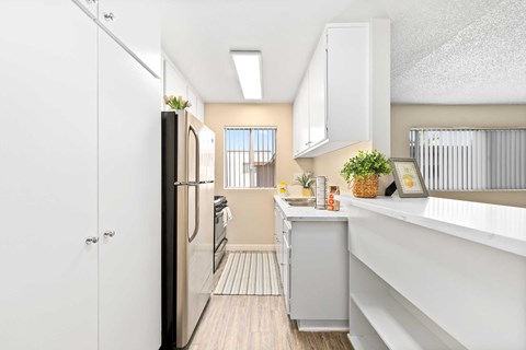 A kitchen with white cabinets, stainless front appliances, quartz countertops, and a small window with blinds.