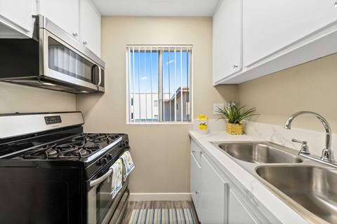 Kitchen area with stainless front appliances, quartz countertops, white countertops, and a small window with blinds.