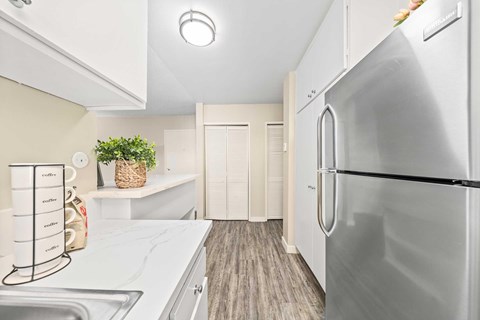A modern kitchen with a stainless steel front fridge, beige walls, quartz countertops, and white cabinets.