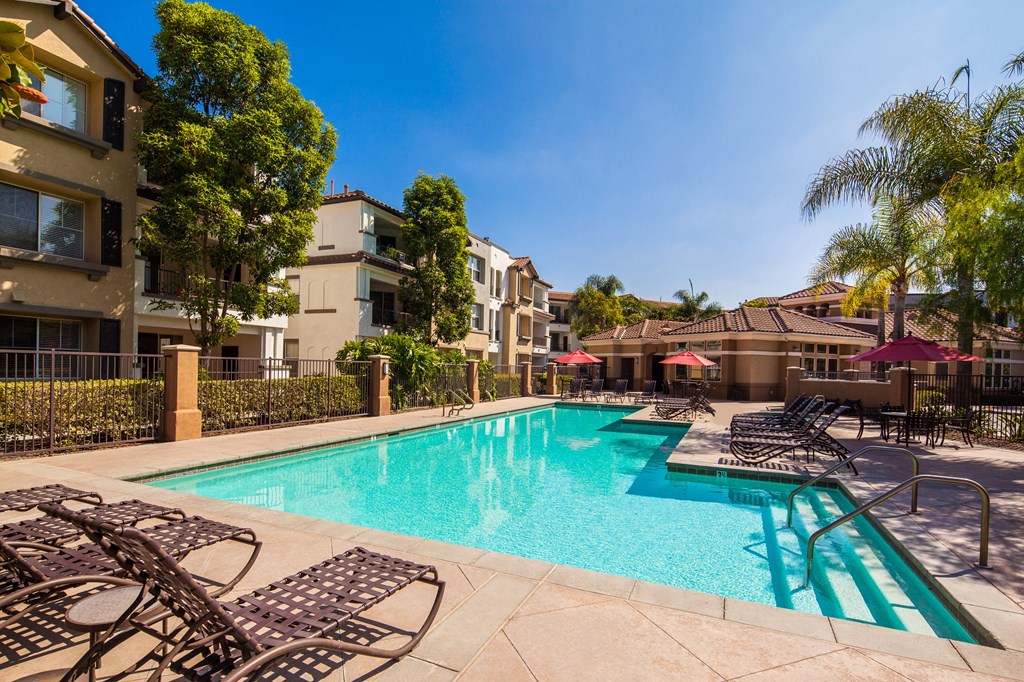 a swimming pool with chairs and umbrellas in front of an apartment building