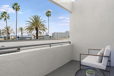 A white chair with a cushion is placed on a balcony with a table holding a plant.