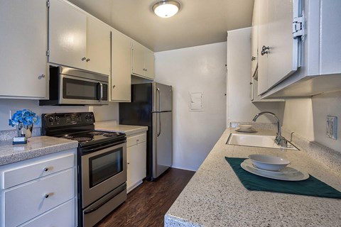 A kitchen with white cabinets, Formica counters, stainless front appliances, and hardwood style vinyl flooring.