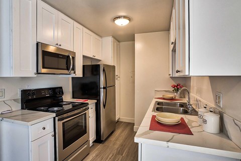 A kitchen with white cabinets, Formica counters, stainless front appliances, and hardwood style vinyl flooring.