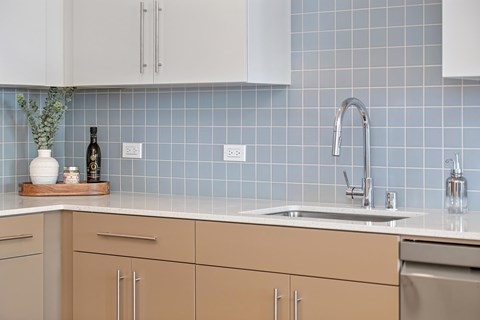 A kitchen with a blue tile backsplash and a white sink.
