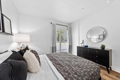 A bedroom with a large bed, a dresser, and a round mirror on the wall.