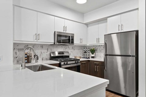 The Elinor's two bedroom modern kitchen with a stainless steel appliances, white and ebony colored cabinets, and quartz white countertops.
