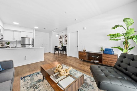 A modern living room with hardwood plank flooring, a coffee table, seating area, and a small dining room table.