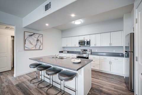 A modern kitchen with wood style plank flooring, white walls, grey countertops, and white cabinets.