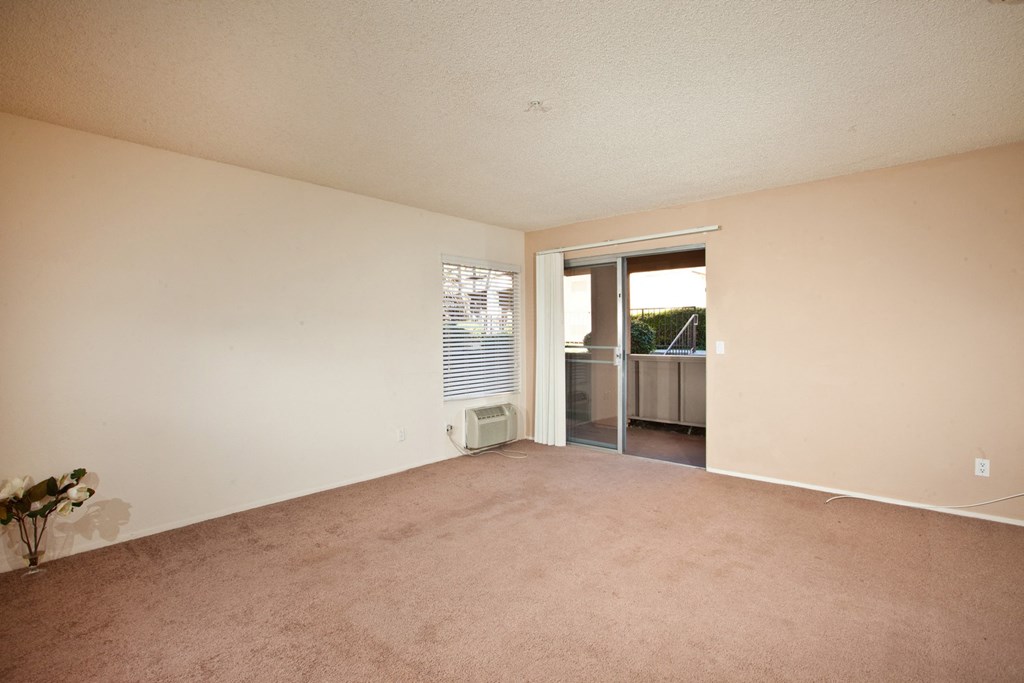 a living room with beige carpet and a sliding glass door to a balcony