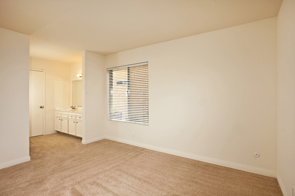 a spacious living room with white walls and carpeting and a bathroom