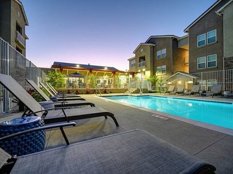 A swimming pool surrounded by lounge chairs and apartment buildings.