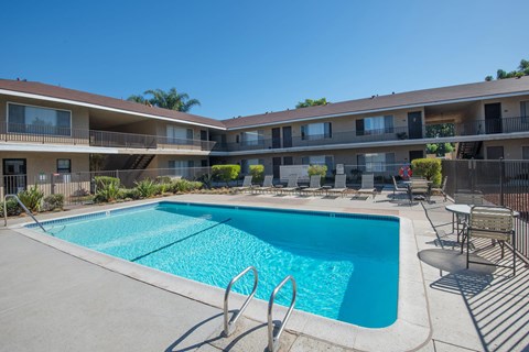 The gated swimming pool area with lounge chairs surrounding. The apartment building is in the background.