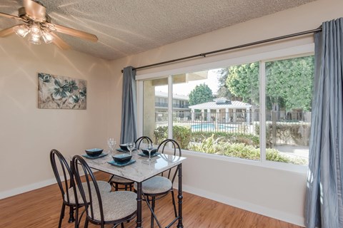 The dining room area with a large window that looks out to the pool area, premium wood style flooring, and a ceiling fan with a light. The area with stage with curtains, a table, and 4 chairs.