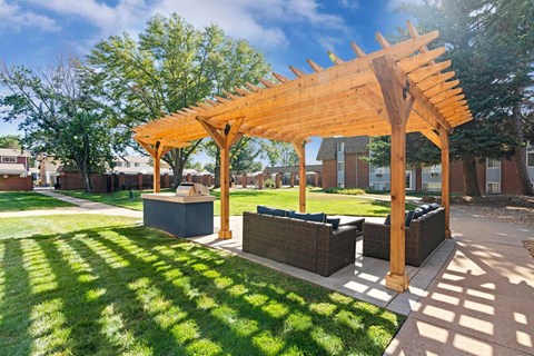 A wooden pergola is over bench seating in a grassy area.