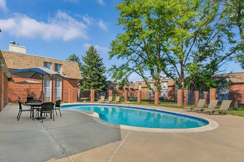 A pool surrounded by a patio area and chairs within a brick apartment complex.