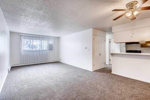 A spacious living room with a ceiling fan and a window with blinds.