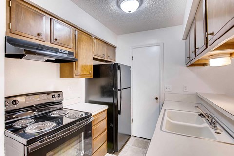 A kitchen with a black refrigerator, stove, wood cabinets, and oven.