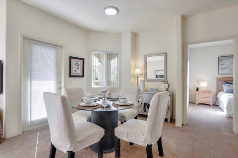 A dining room with a glass table and white chairs.