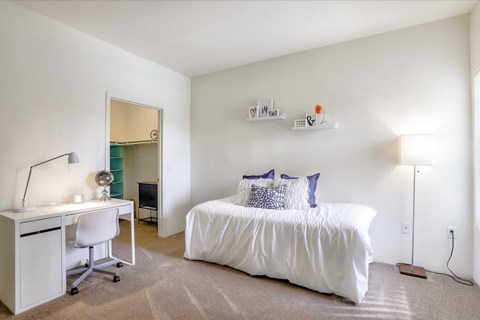A bedroom with a white bed and a desk with a computer.