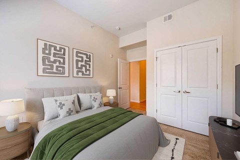 A bedroom with a bed, nightstands, and paintings hanging over the bed. a door in the back leads to a bathroom
