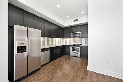 The kitchen with stainless front appliances, vinyl wood flooring, ebony dark cabinets, ceramic tile backsplash, and under cabinet lighting.