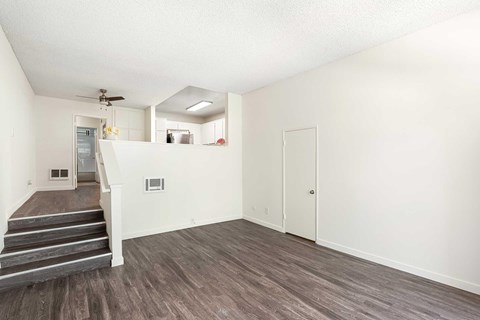 A living room with white walls, vinyl wood flooring, and a few stairs to get to the dining room and kitchen area.