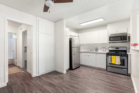 A kitchen with white cabinets, stainless front appliances, a ceiling fan, and vinyl wood flooring.