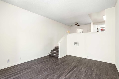 A living room with white walls, vinyl wood flooring, and a few stairs to get to the dining room and kitchen area.