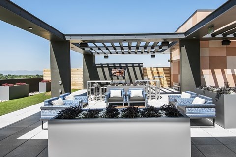A modern outdoor seating area with a planter, tv and bar stools and tables