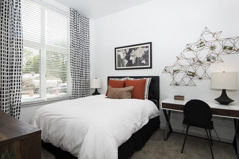 A bedroom with a bed, desk, chair, window, and a wall art.