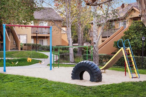 A playground with a slide, swings, and a tire swing set.